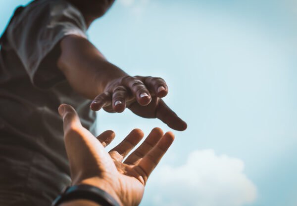One hand extends from the bottom of the shot with a hand reaching toward it from the top of the shot