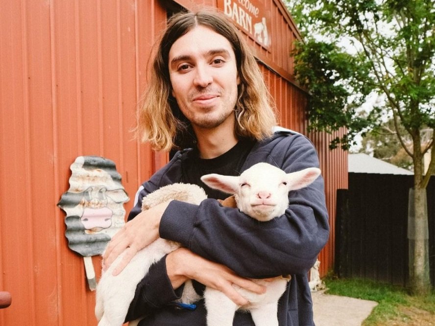 Earthling Ed holding a lamb in his arms outside a red barn