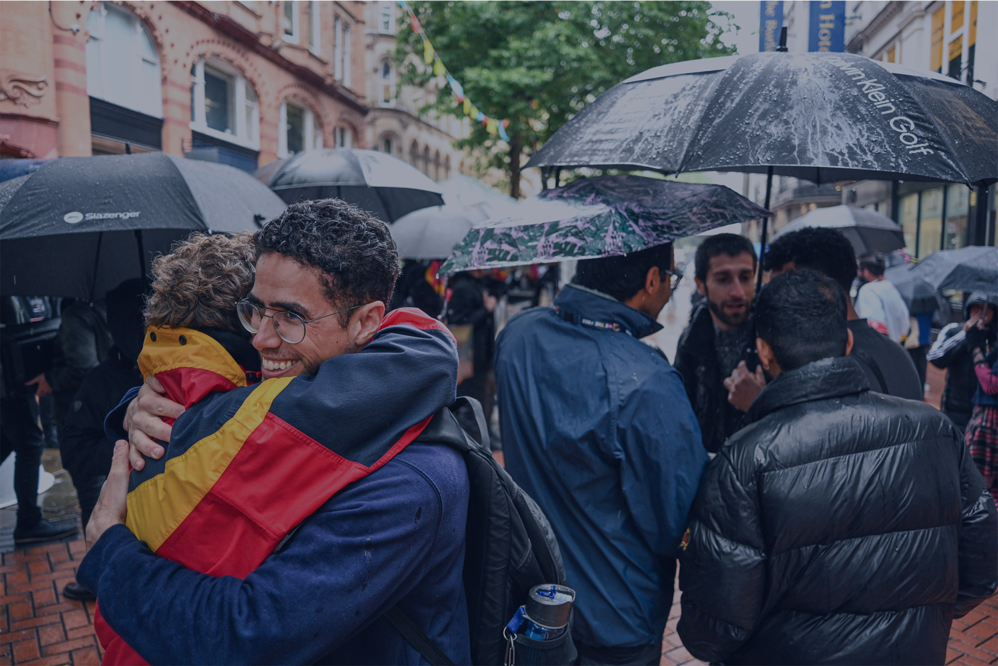 Activists embracing under umbrellas at a rainy street event
