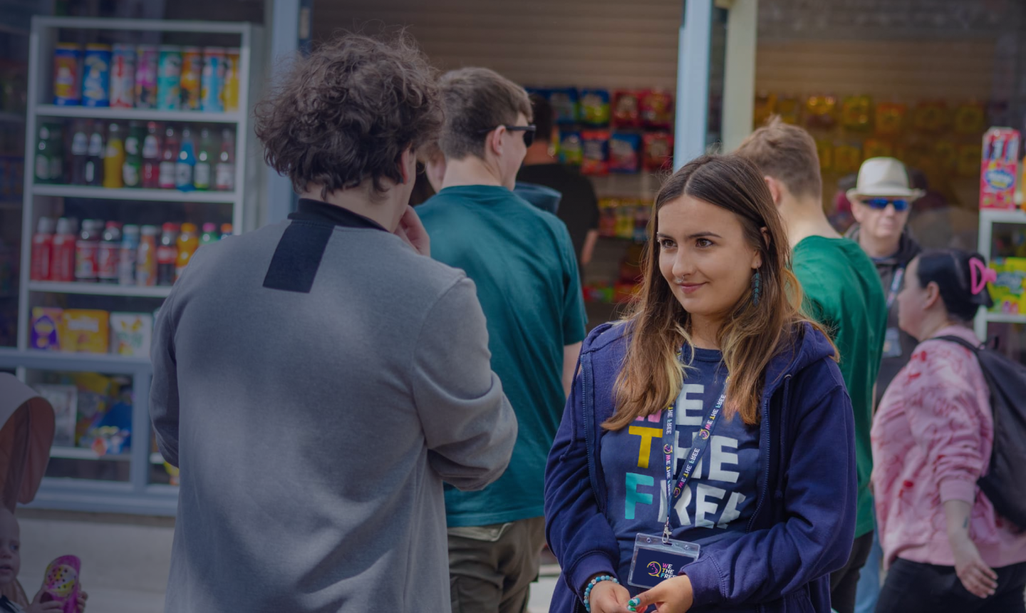 A WTF volunteer in a We The Free shirt and lanyard talking with a passer-by at a street outreach stall