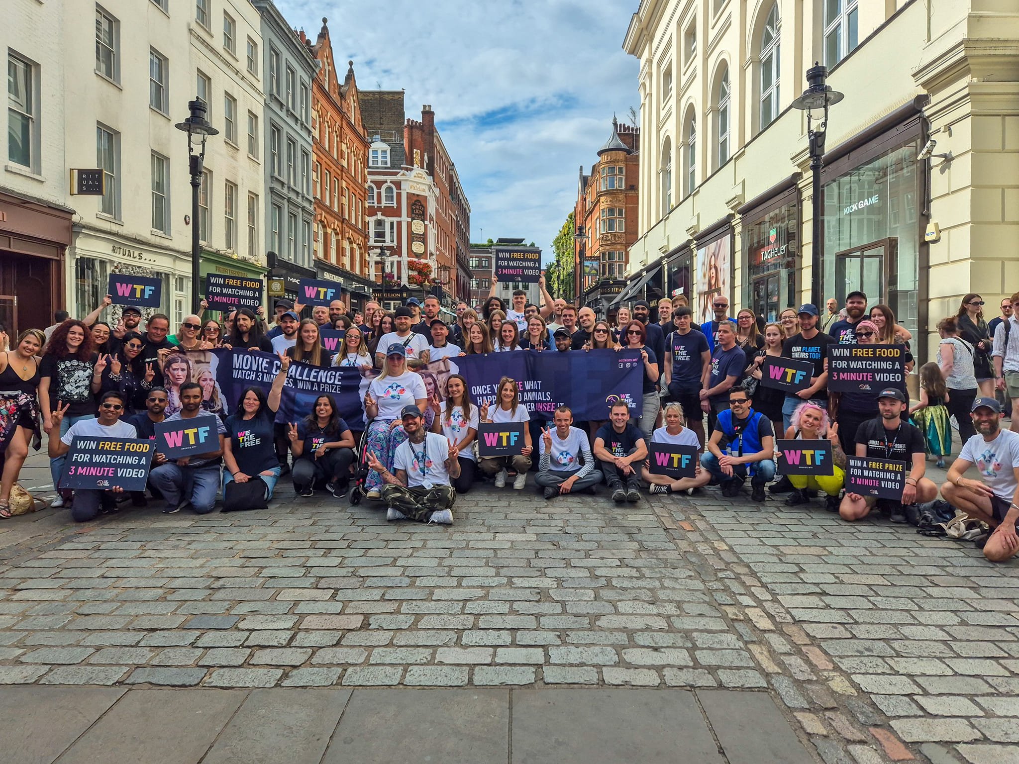 A large group of WTF activists posing together in a cobbled street with Movie Challenge banners and WTF signs