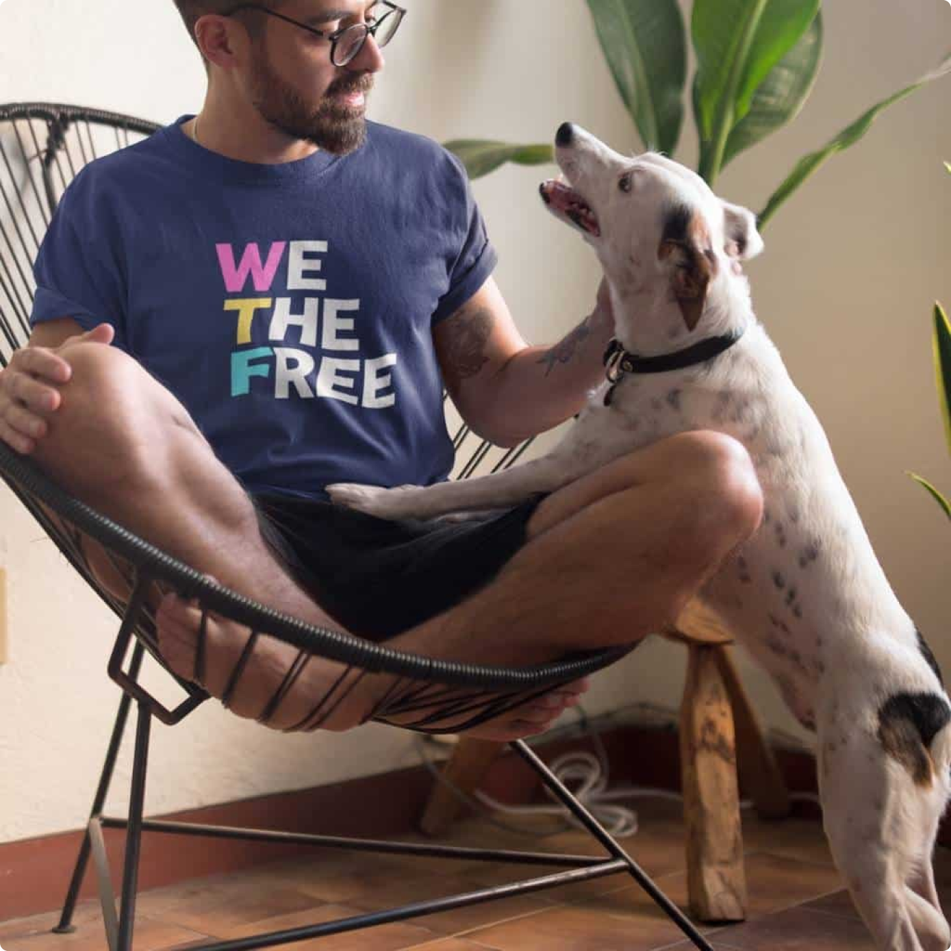 A man in a navy We The Free t-shirt sitting in a chair with a dog resting its paws on his knee
