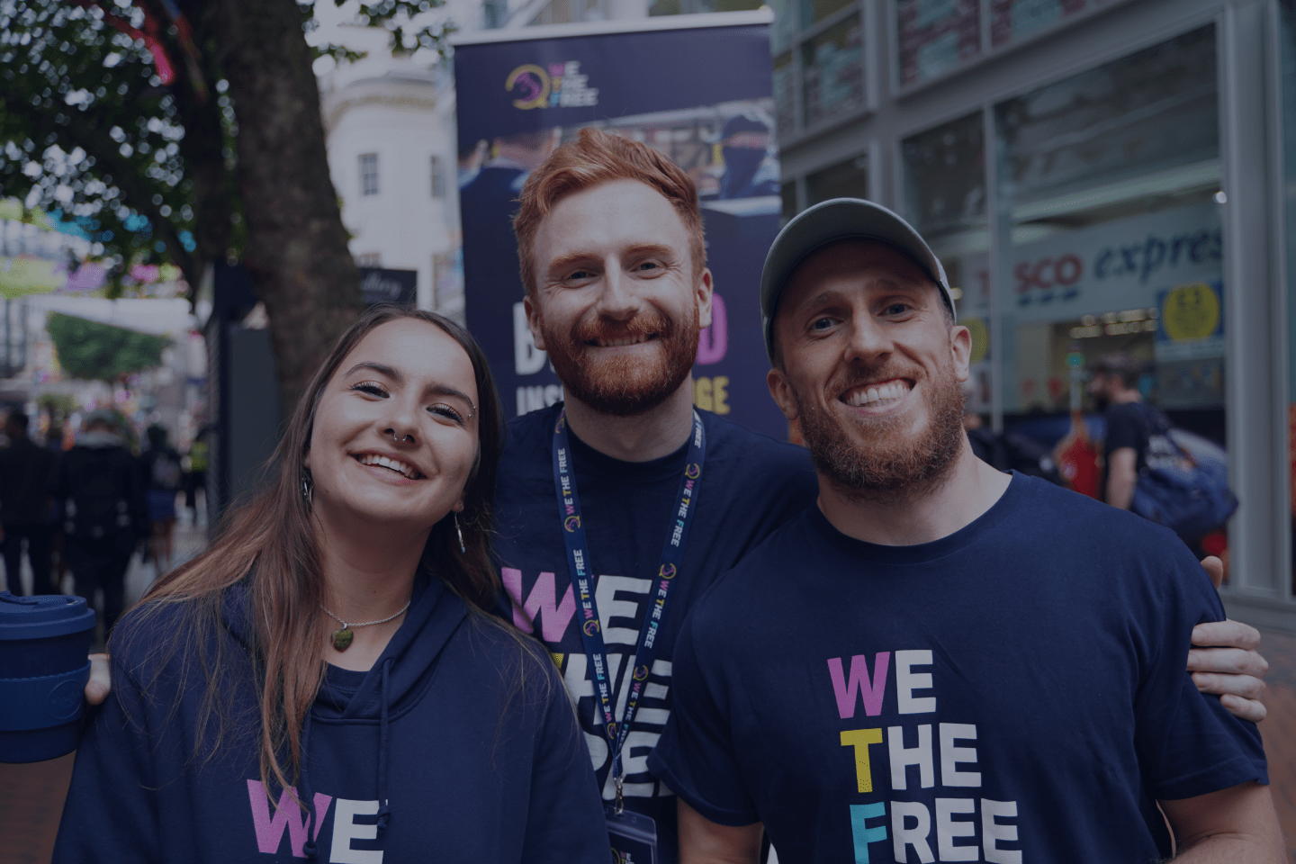 Three We The Free volunteers in branded shirts at a street stall