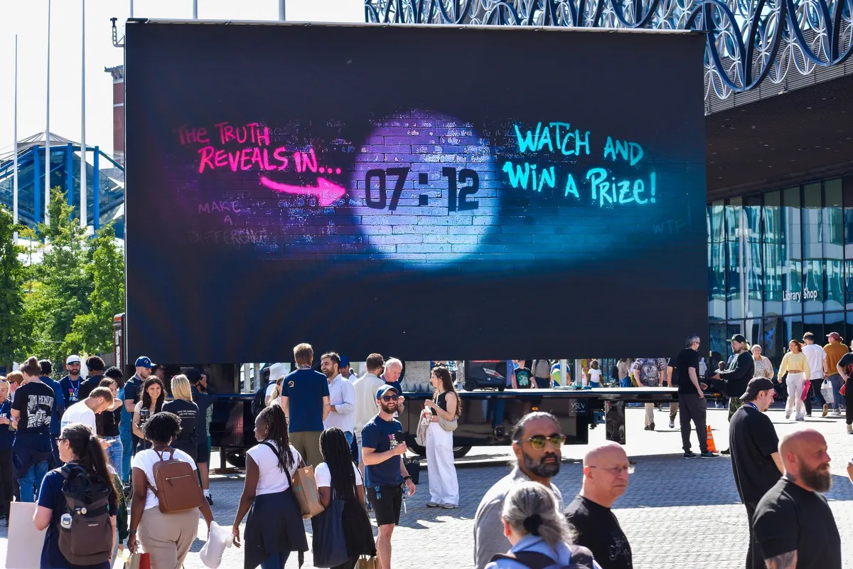 A giant screen on a truck in Birmingham city centre counting down to a film, with crowds of people walking past in the sun